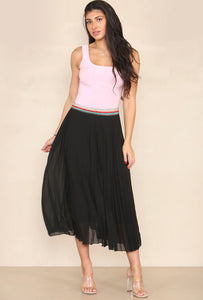 Model wearing a fully lined black pleated maxi skirt with a sparkly rainbow striped elasticated waistband 