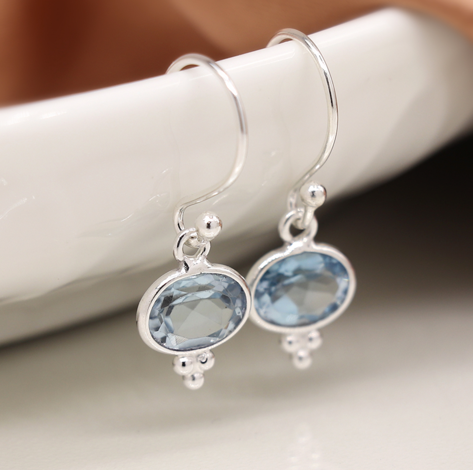 Photo of a pair of sterling silver drop earrings with faceted topaz and three small silver dot detail at base and fine silver hooks