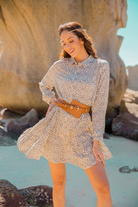 Model wearing a shirt dress in a tiered boho style and cream and brown leopard print with long sleeves and a waist belt