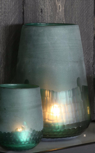 Green glass lanterns with lit candles on a shelf