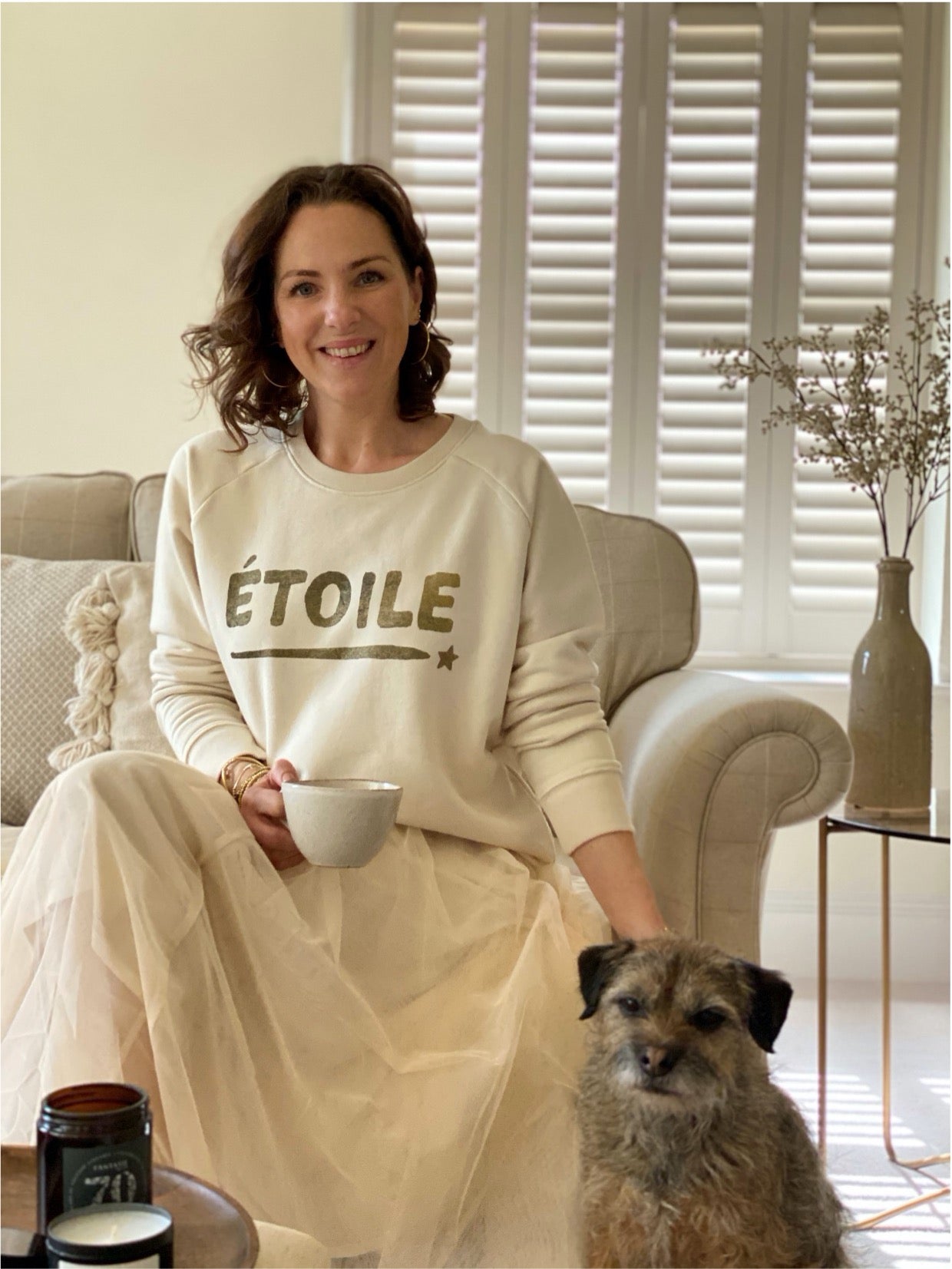 Model wiearing etoile star sweatshirt in cream and gold holding cup of coffee sitting with a dog 