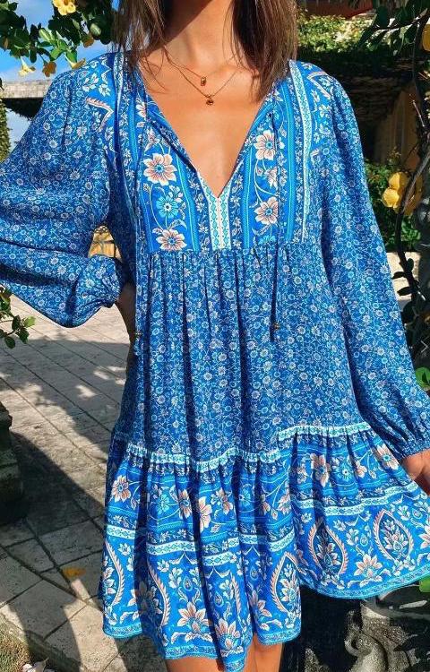 Model wearing a boho mini dress in blue floral print with v tie neck and long bell sleeves