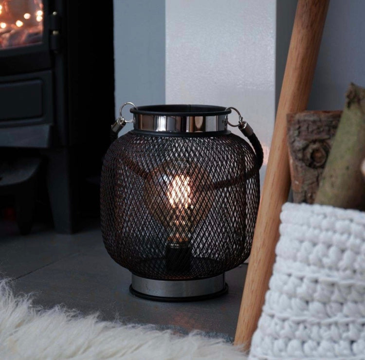 Black and chrome mesh lantern with battery operated LED bulb by fireplace
