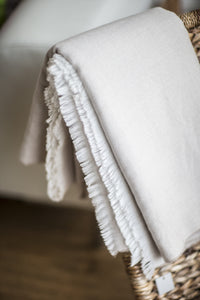 A natural throw with tassel fringing draped over a chair 